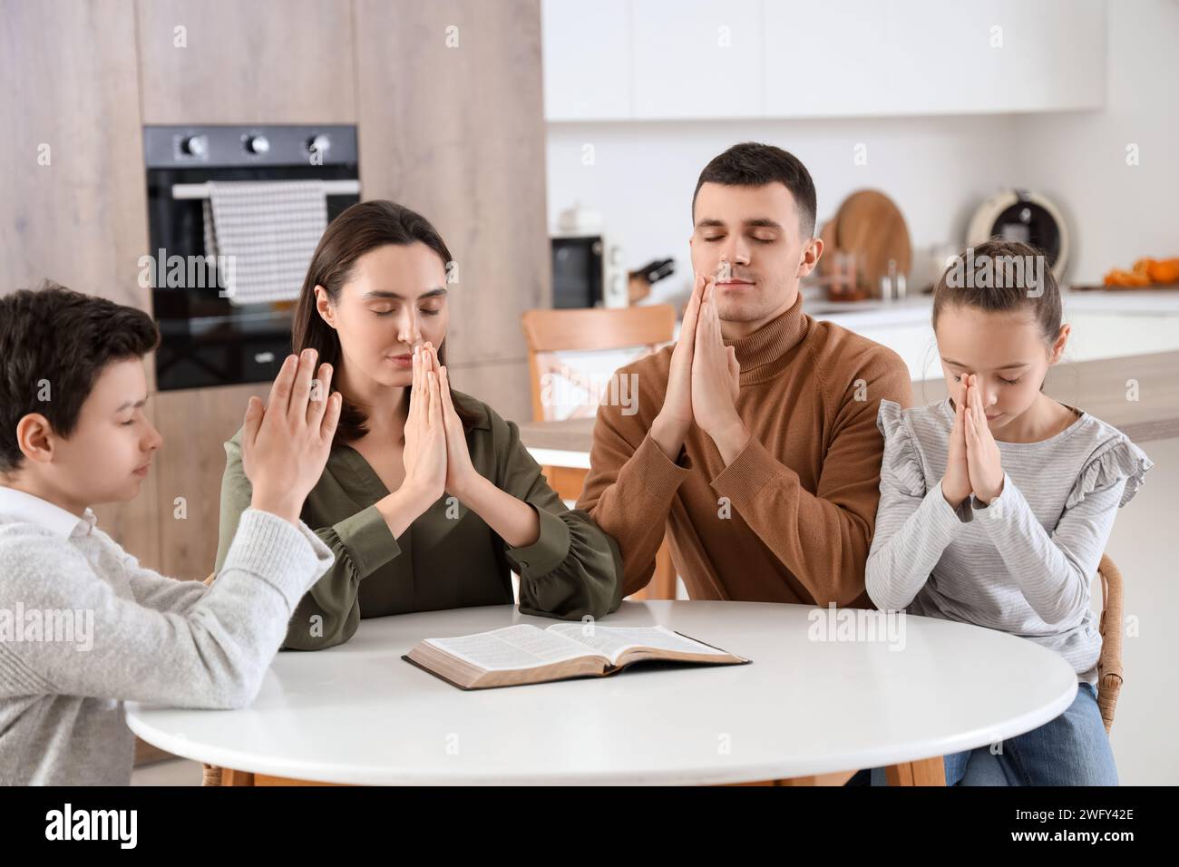 Family praying with Holy Bible on table in kitchen Stock Photo