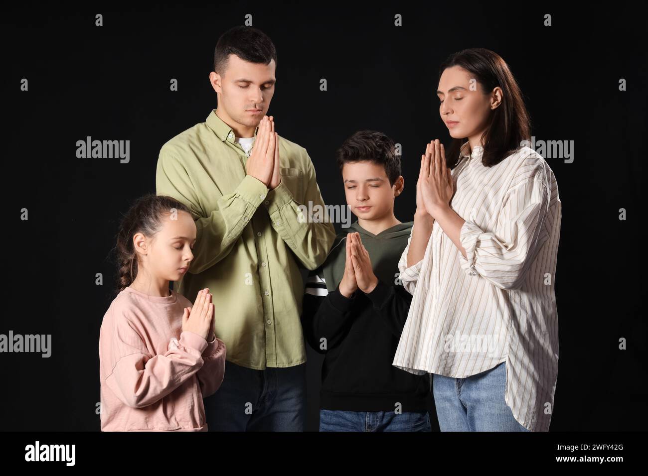 Family praying together on dark background Stock Photo