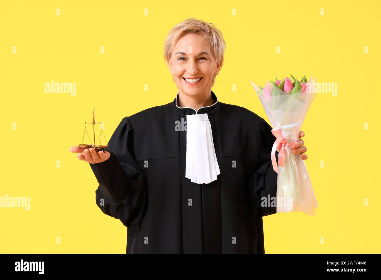 Mature female judge with tulips and justice scales on yellow background ...