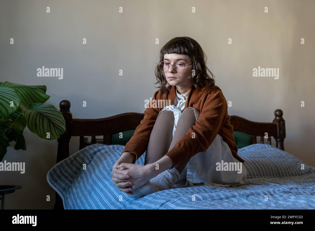 Sad upset teen girl in puberty period sitting on bed feeling procrastination, depression, loneliness Stock Photo
