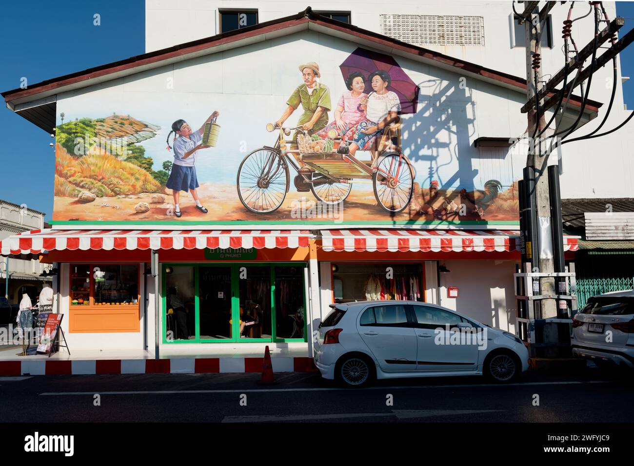 A mural in Phuket Town, Phuket, Thailand, depicting a trishaw driver of old with two female passengers and a young girl with a tiffin box (lunch box) Stock Photo