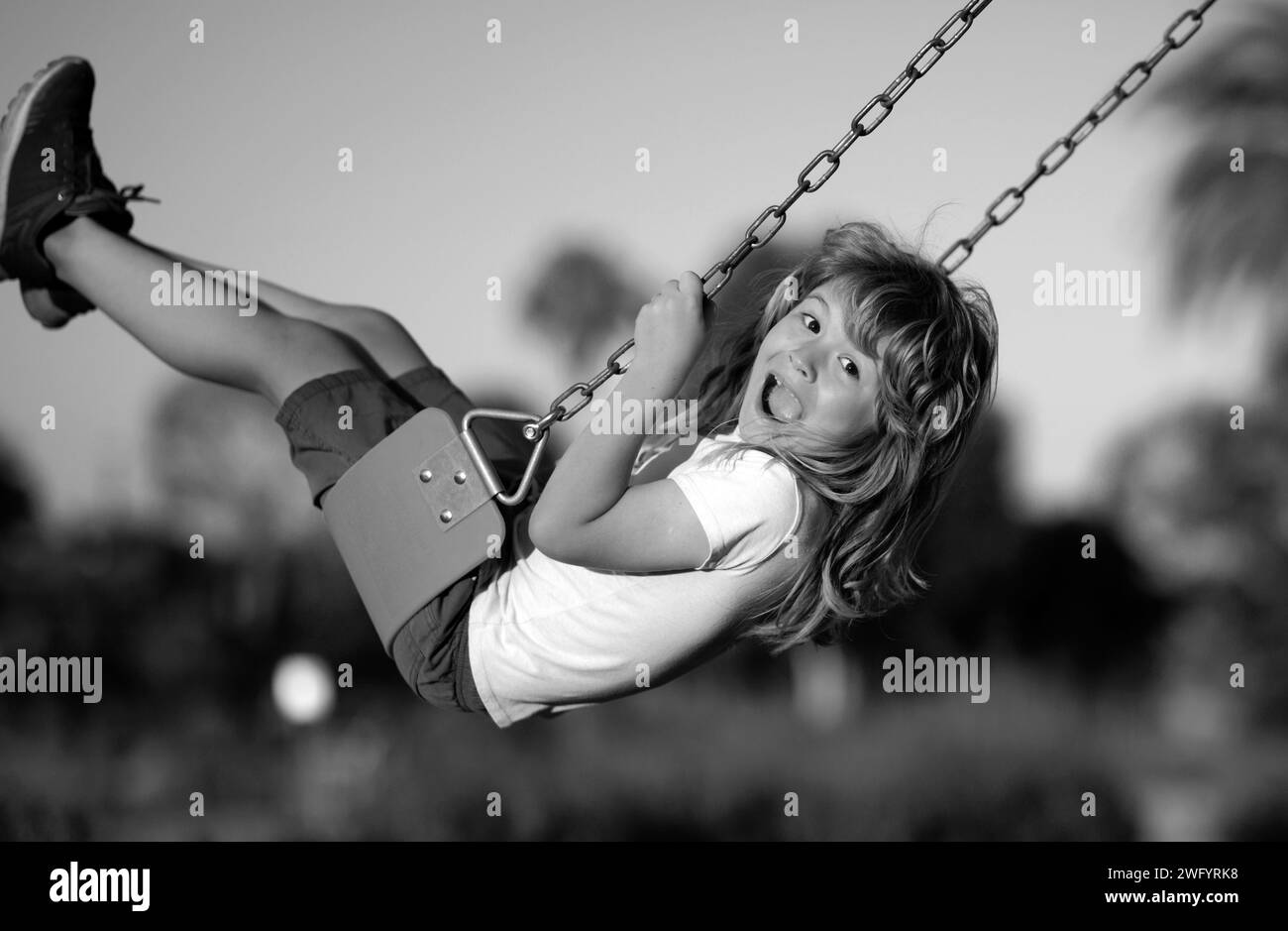 Emotional portrait of a child in the playground. Outdoor kids activity. Little boy having fun on a swing on the playground in public park on autumn da Stock Photo