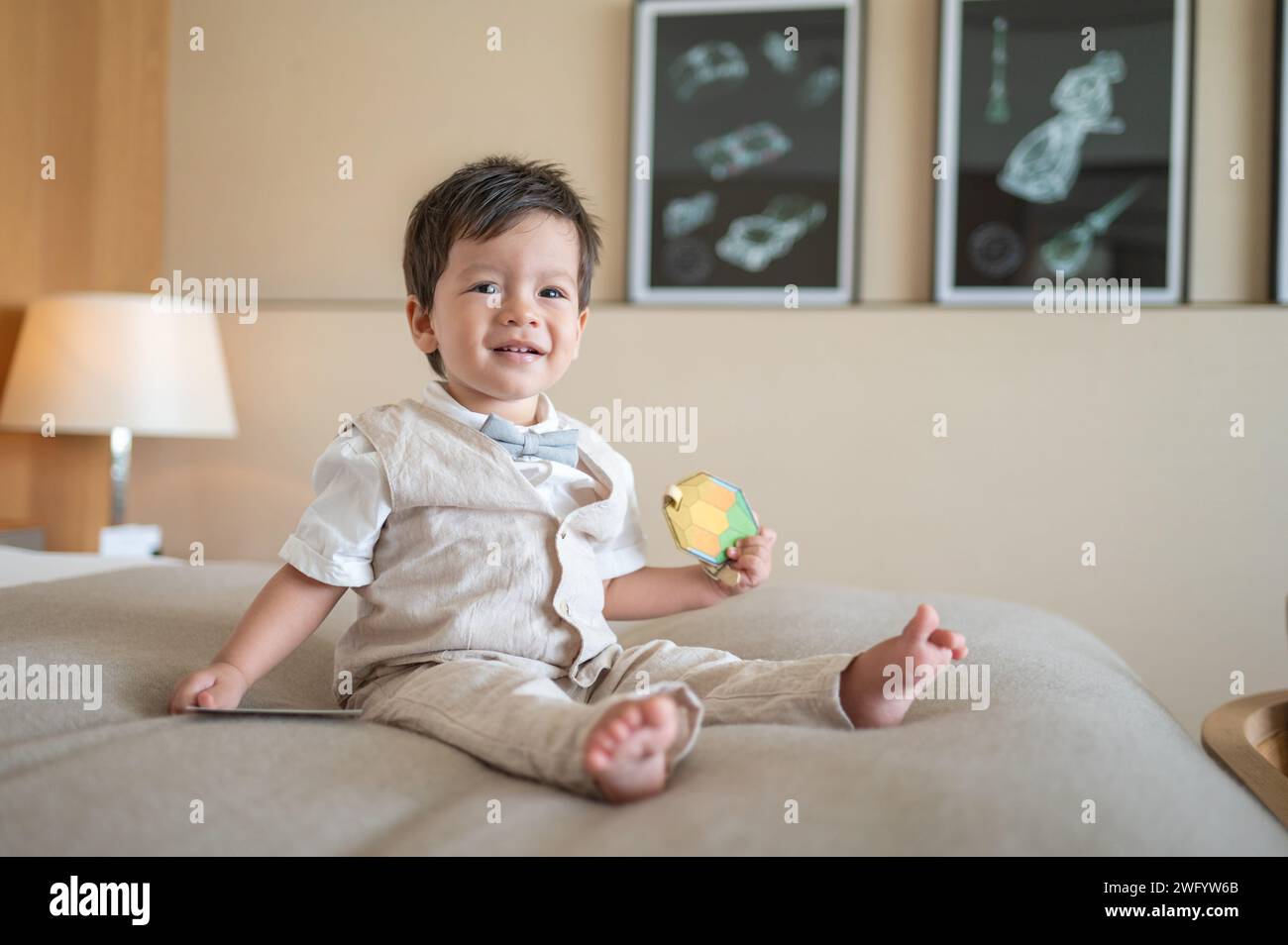 Cute one year old multiracial baby boy celebrating his first birthday at home. He is dressed in a beige summer linen suit with a bright bow tie. He is Stock Photo