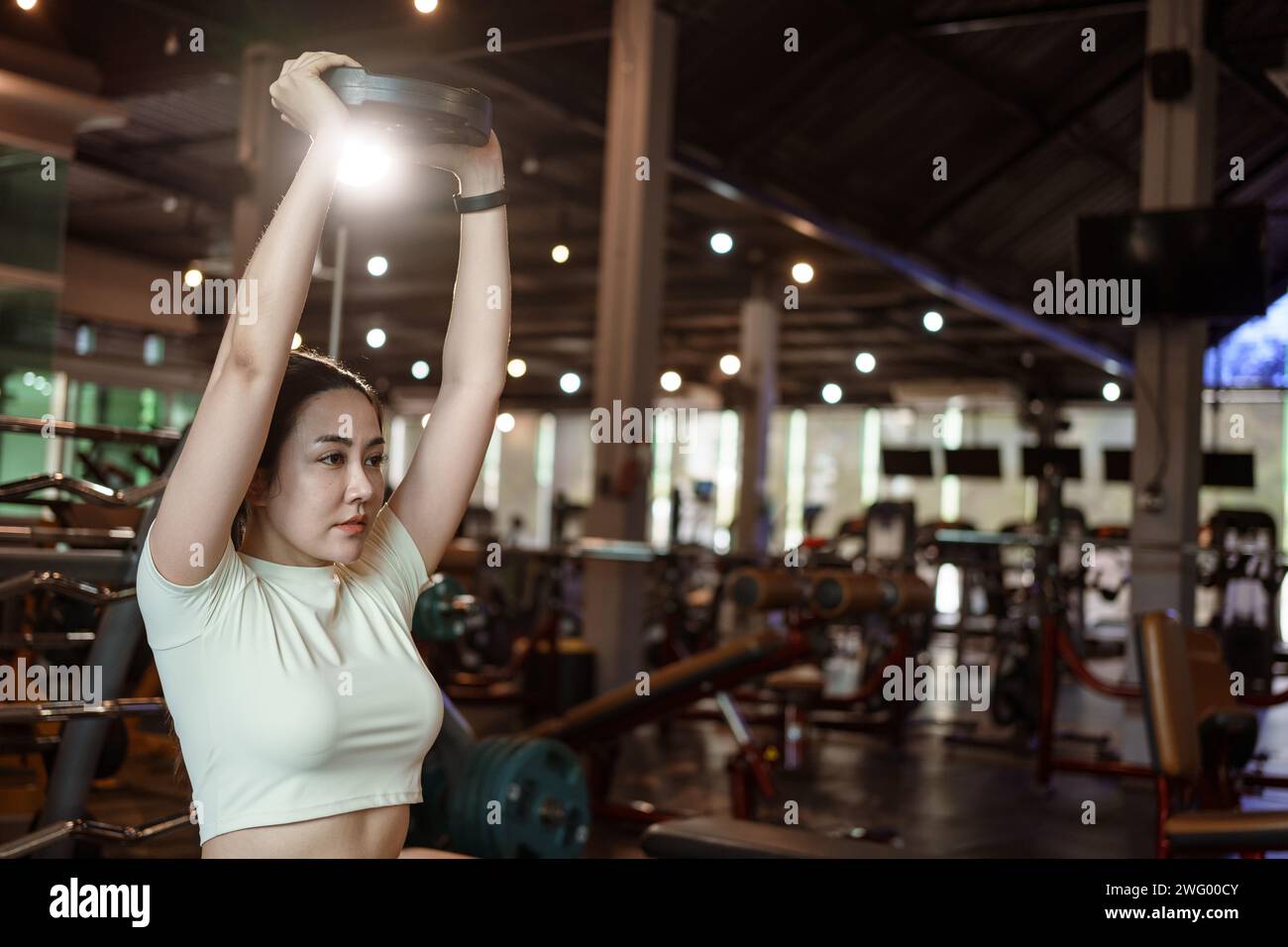 Sporty woman exercising with weight plate in the gym. Stock Photo