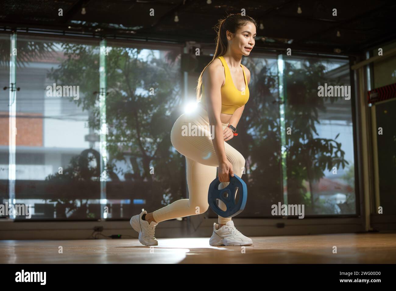 Sporty woman exercising with weight plate in the gym. Stock Photo