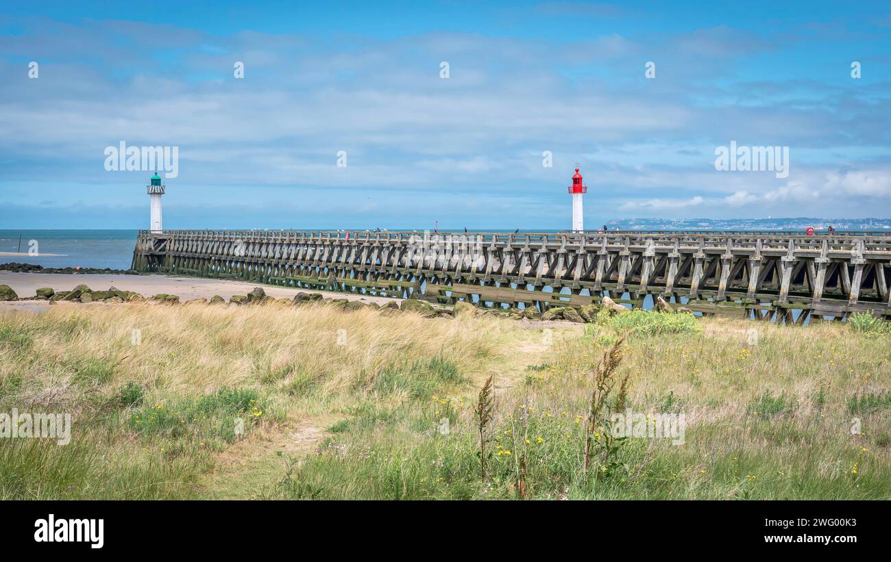 A wooden pier beside the sea with a vibrant red and white lighthouse atopc Stock Photo