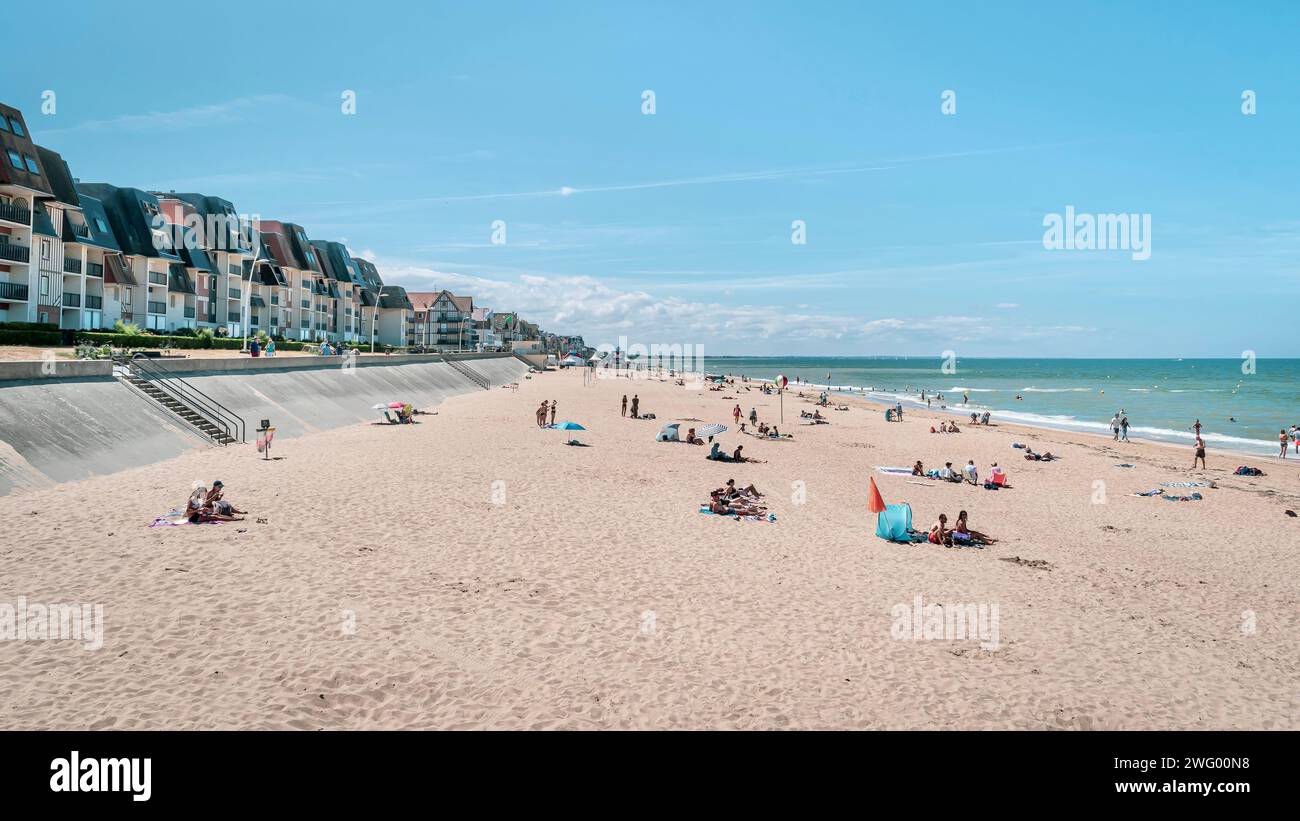 Some people enjoying a sunny day on the beach with tall apartment ...