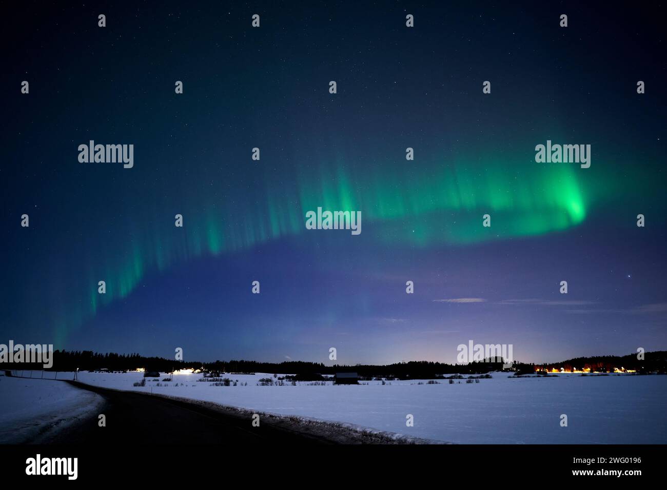 The Northern lights over snowy landscape at night with vibrant blue and green hues. Stock Photo