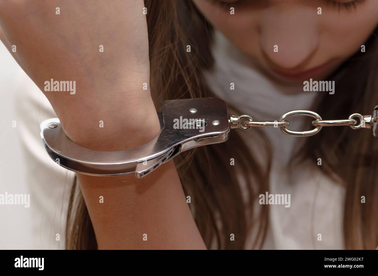 A teenage girl looks at her handcuffed hands. Concept: Juvenile delinquent, criminal responsibility of juveniles. Stock Photo