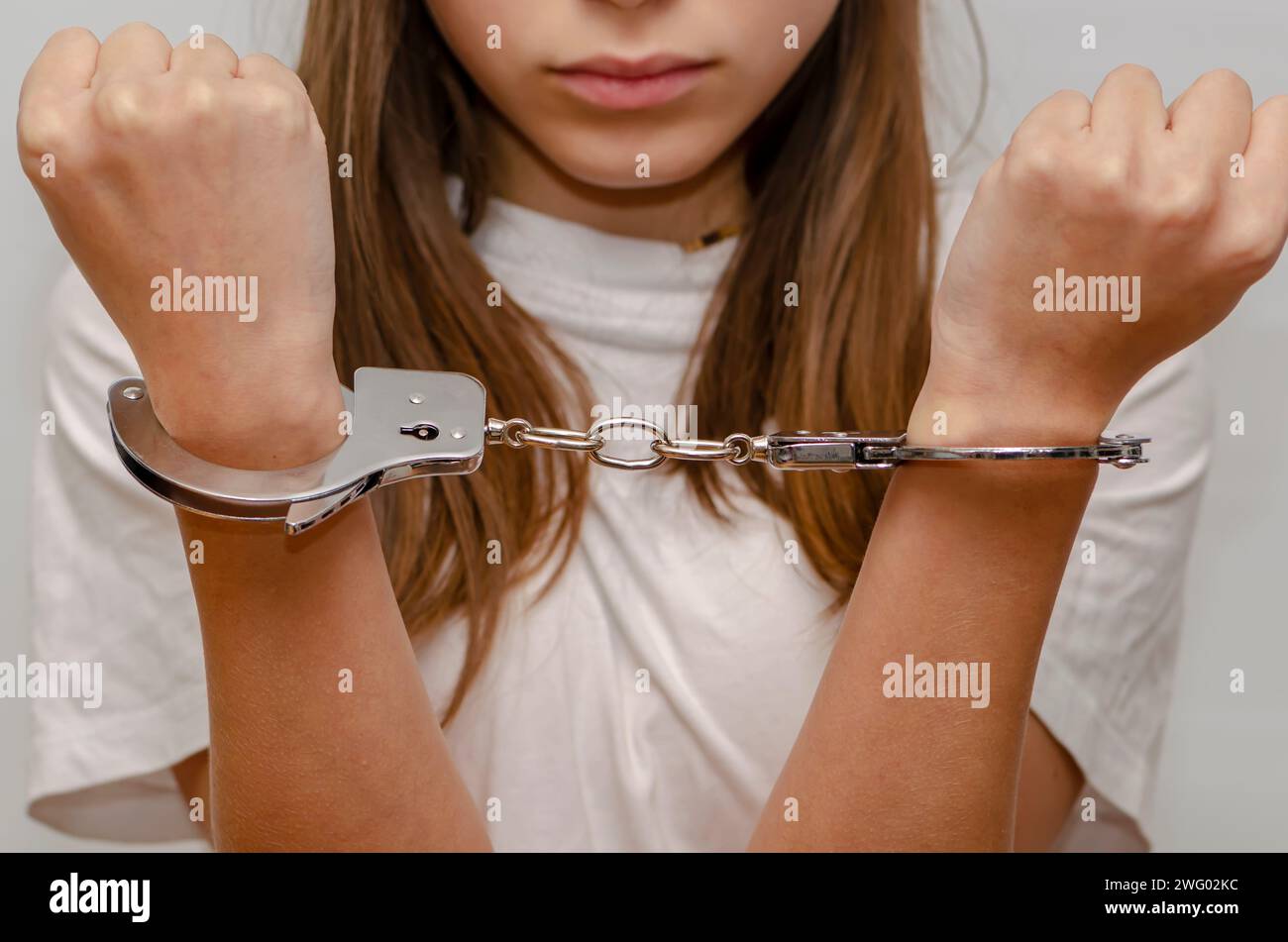 Teenage girl in handcuffs on gray background. Juvenile delinquent, criminal responsibility of juveniles. Stock Photo