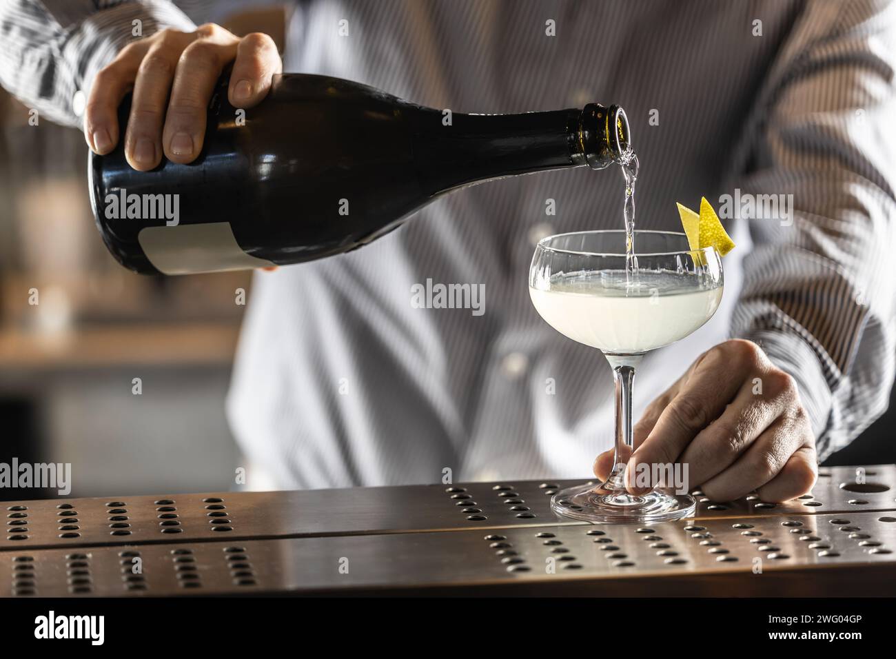 A bartender pours champagne or prosecco into a French 75 cocktail drink. Stock Photo