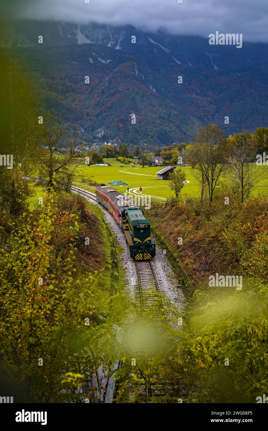 Diesel train in the valley in Slovenia, behind it mountains and autumn forest Stock Photo