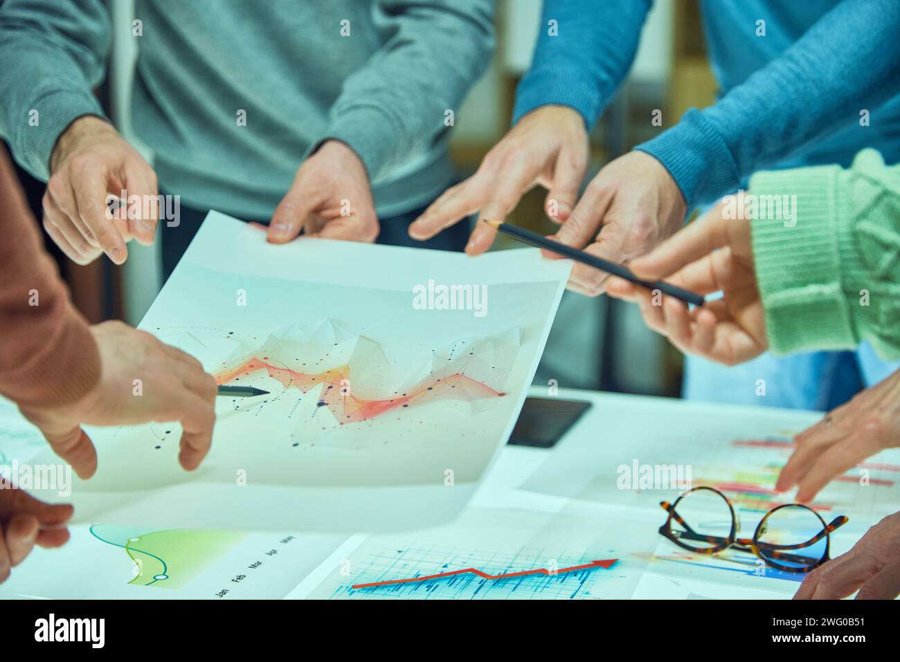 Individuals examining and discussing a complex data visualization sheet among other graphs. Collages working with analytical graphs Stock Photo