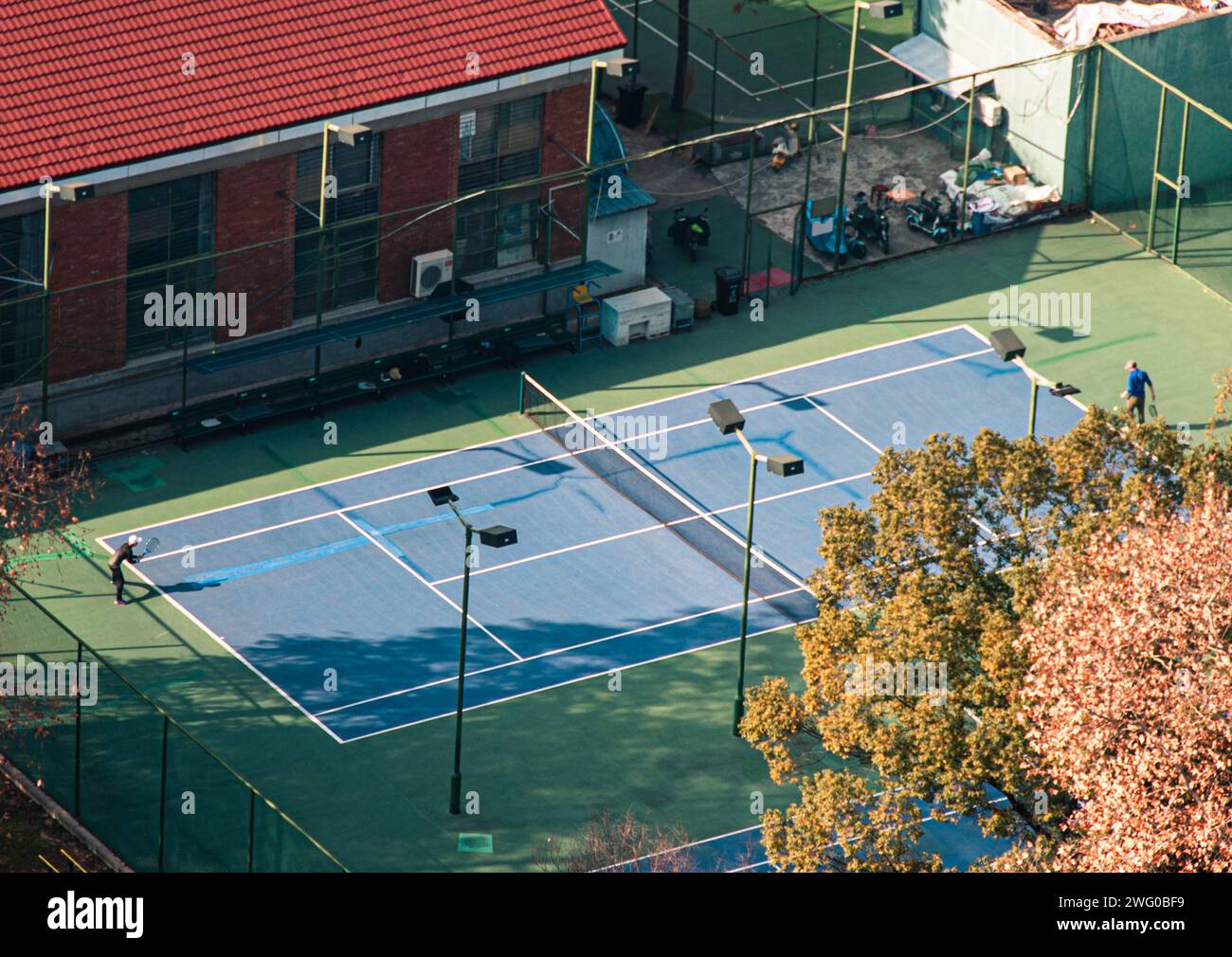 Two individuals engage in a friendly game of tennis on a court beneath a towering architectural structure Stock Photo