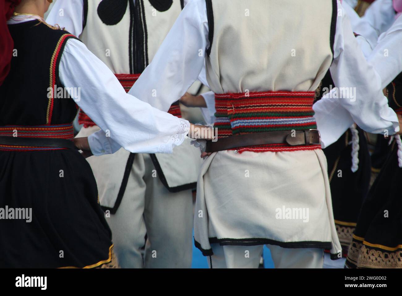 Group of individuals in elegant attire exchanging glances at a social gathering: Serbian folk dancers in a festival Stock Photo