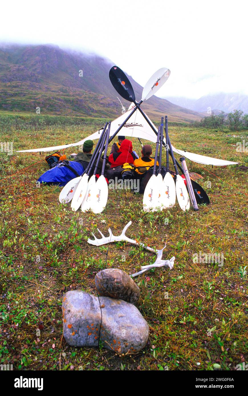 Expedition members relax beneath the tarp on a rainy day along a river, Arctic National Wildlife Refuge, Alaska. Stock Photo