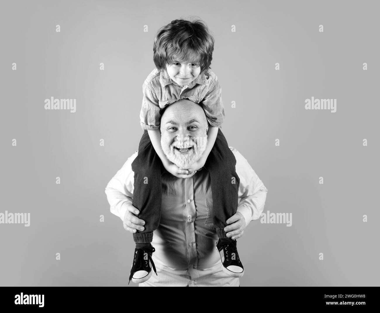 Grandfather and son piggyback ride with funny face isolated on blue in studio. Granddad and cute boy with funny face Stock Photo