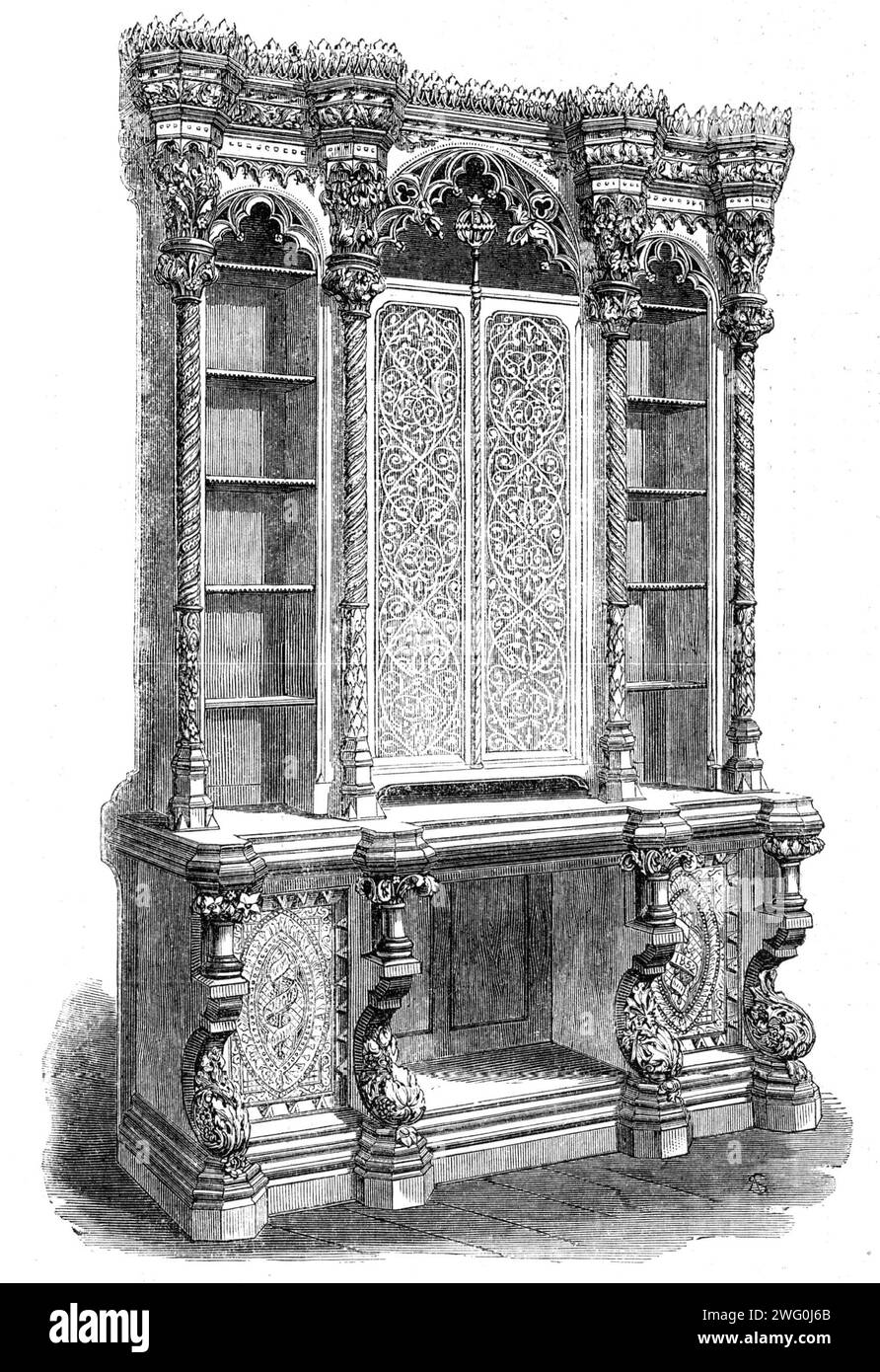 The International Exhibition: bookcase by Hindley and Son, 1862. 'It is carved in light-coloured oak, and is in the mediaeval style: it stands 10ft. 6in. in height, is 7ft. long, and has the centre doors panelled with glass, over which is a light tracery of wood. The end doors below are carved solid and are minutely finished; and the scrolls, which now contain the word Hindley and the date 1862, are destined to receive mottoes. The architectural massing out of the structure is good, and the construction is well considered, support being given where occasion requires; and one feature which is f Stock Photo