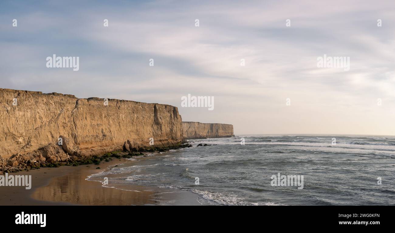 Colorful coastal view of tall cliffs and ocean waves at sunset. Stock Photo