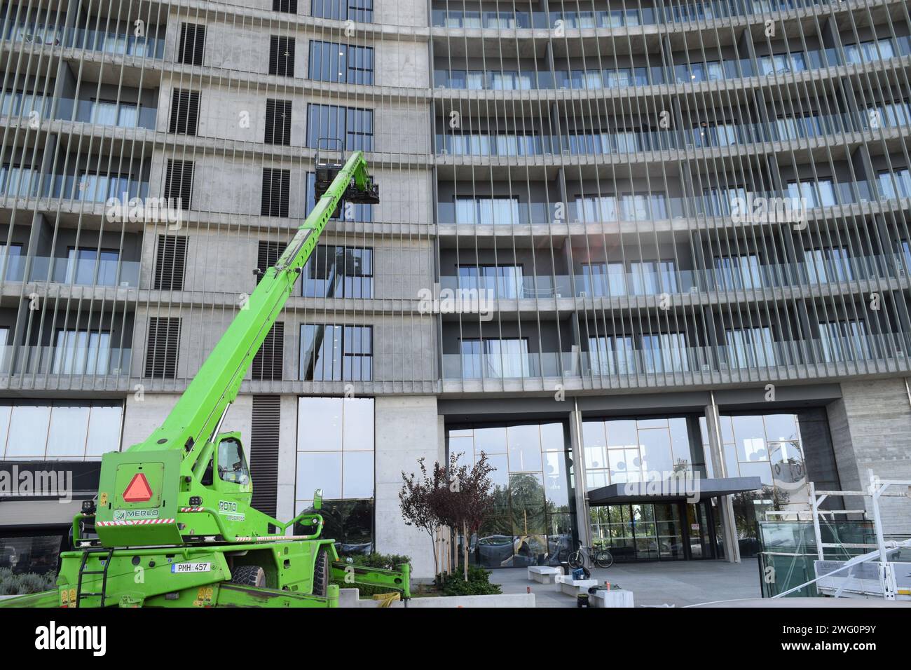 A green telescopic boom lift.There is a worker in the platform,that is doing something on the structure of the building. Stock Photo