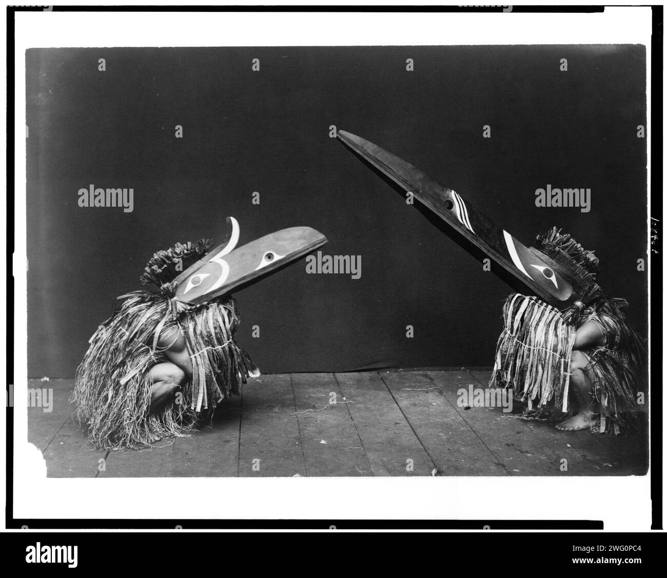 Kotsuis and Hohhug-Nakoaktok, wearing ceremonial dress, with long beaks, on their haunches, dancing(?), c1914. Stock Photo