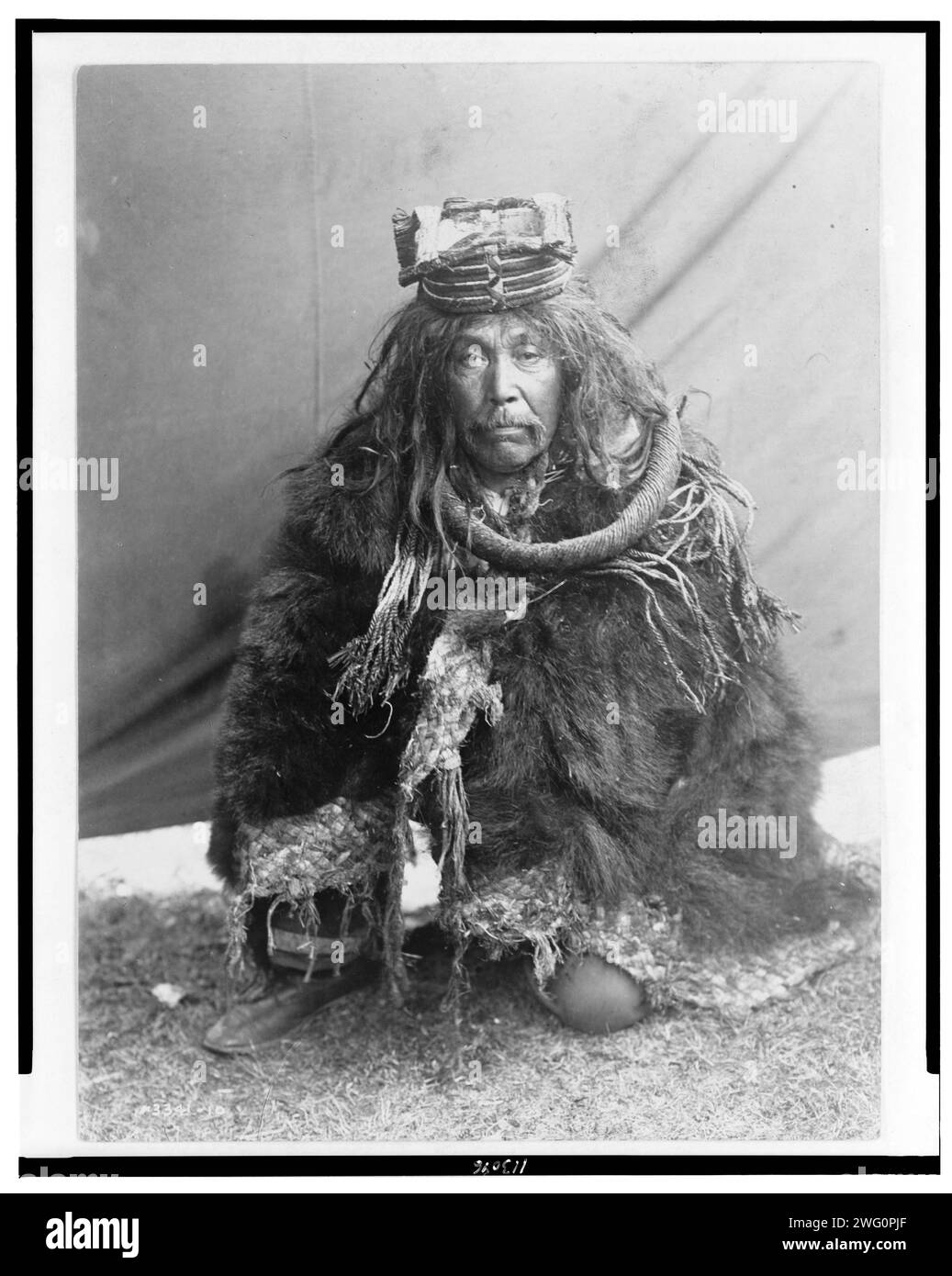 A Hamatsa costume-Nakoaktok, c1910. Kwakiutl man kneeling on one knee dressed in skins, hat and other garments. Stock Photo