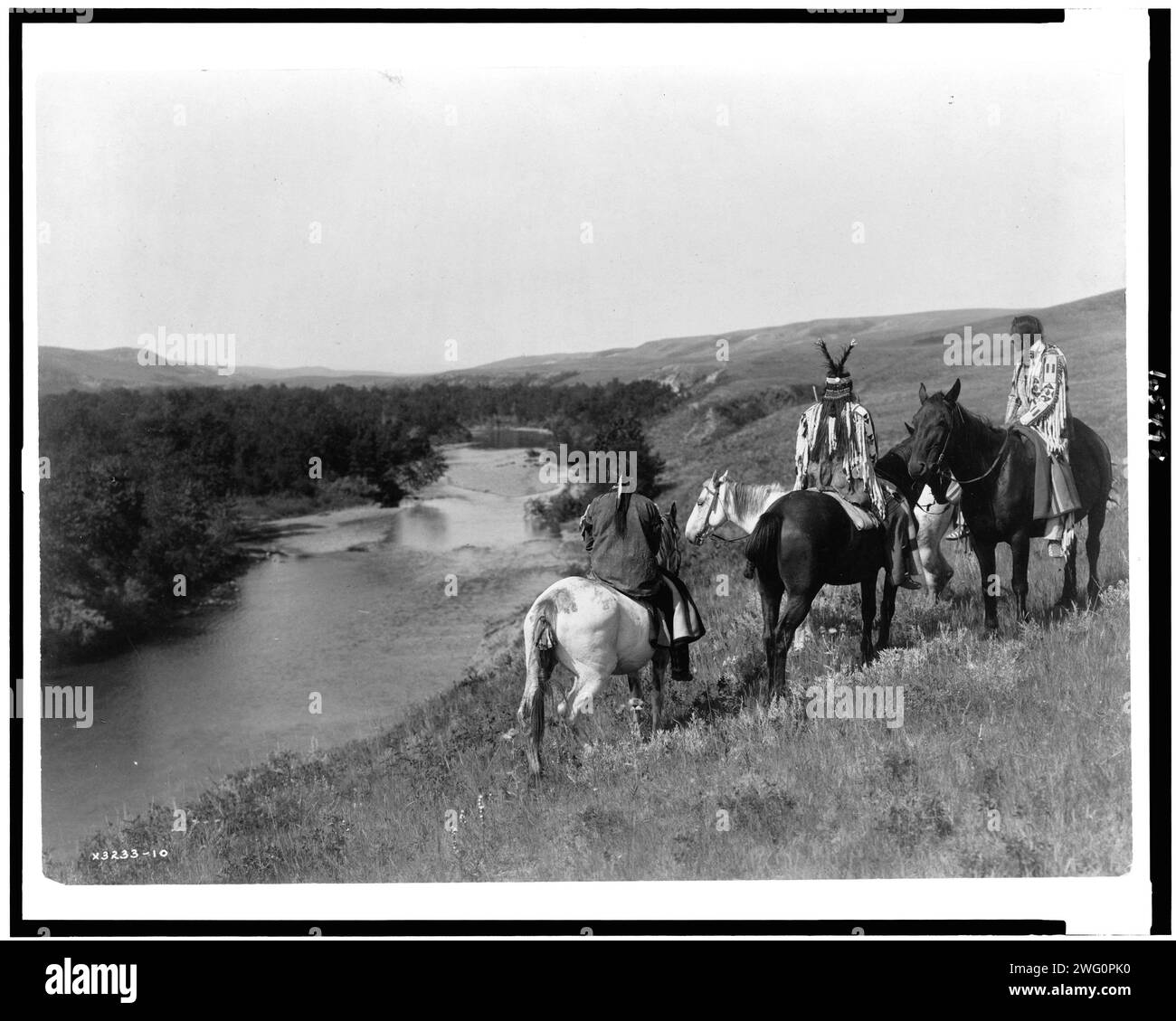 Three Piegan Indians and four horses on hill above river, c1910. Stock Photo