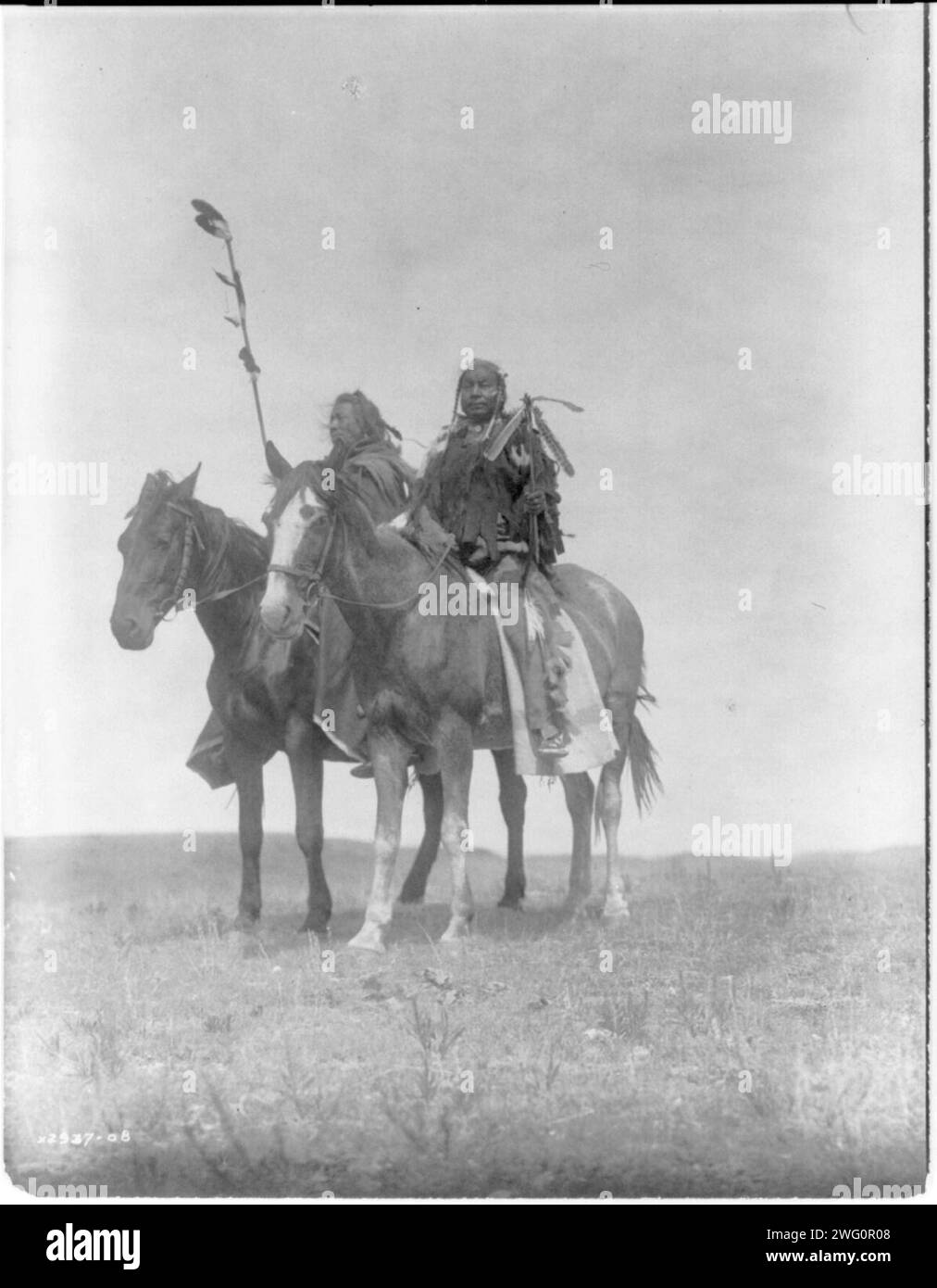 Atsina chiefs, c1908. Two Atsina chiefs on horseback, one with feathered staff and one with a coup stick. Stock Photo