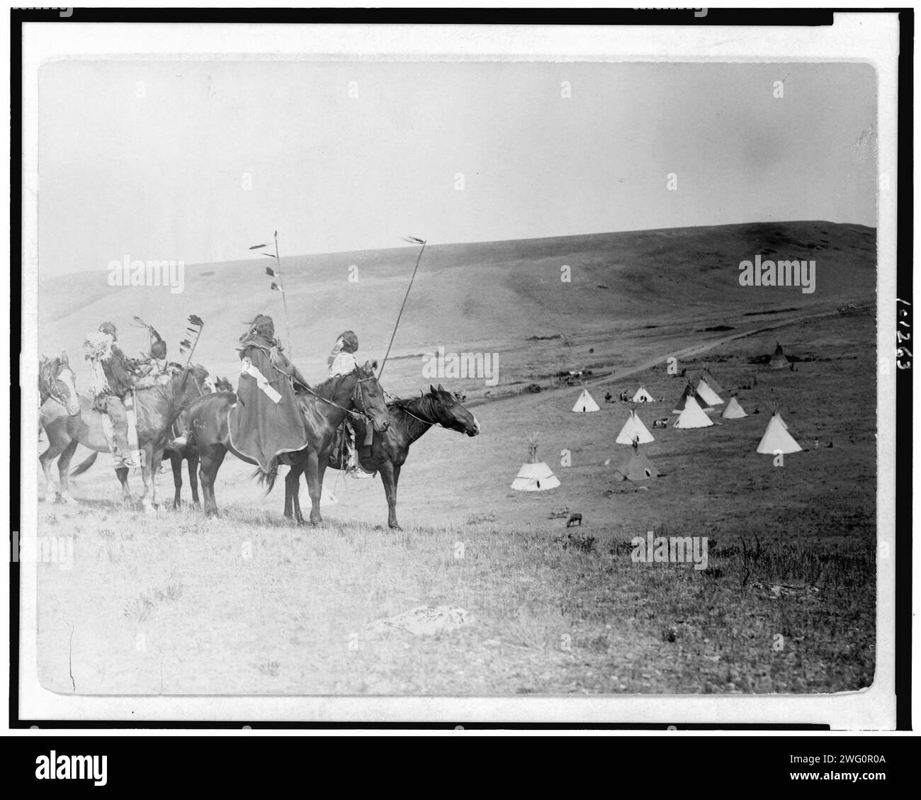War party's farewell-Atsina, c1908. Four Atsina Indians on horseback overlooking tepees in valley beyond. Stock Photo