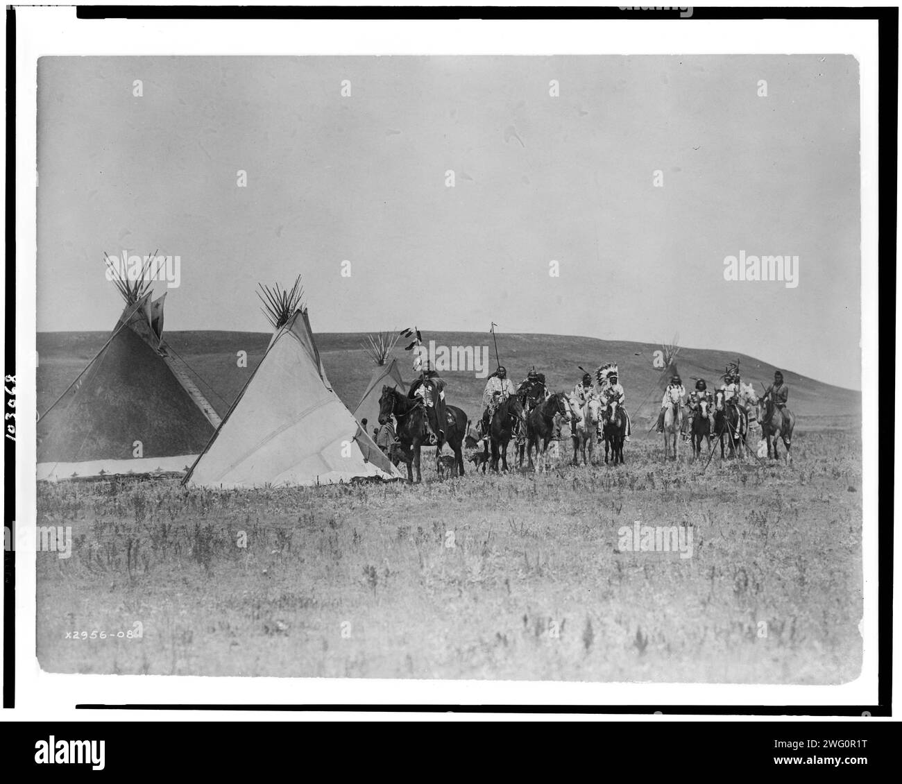 A gathering war party, c1908. Landscape with four tepees, eleven Atsina Indians on horseback, three women, a child, and two dogs, Montana. Stock Photo