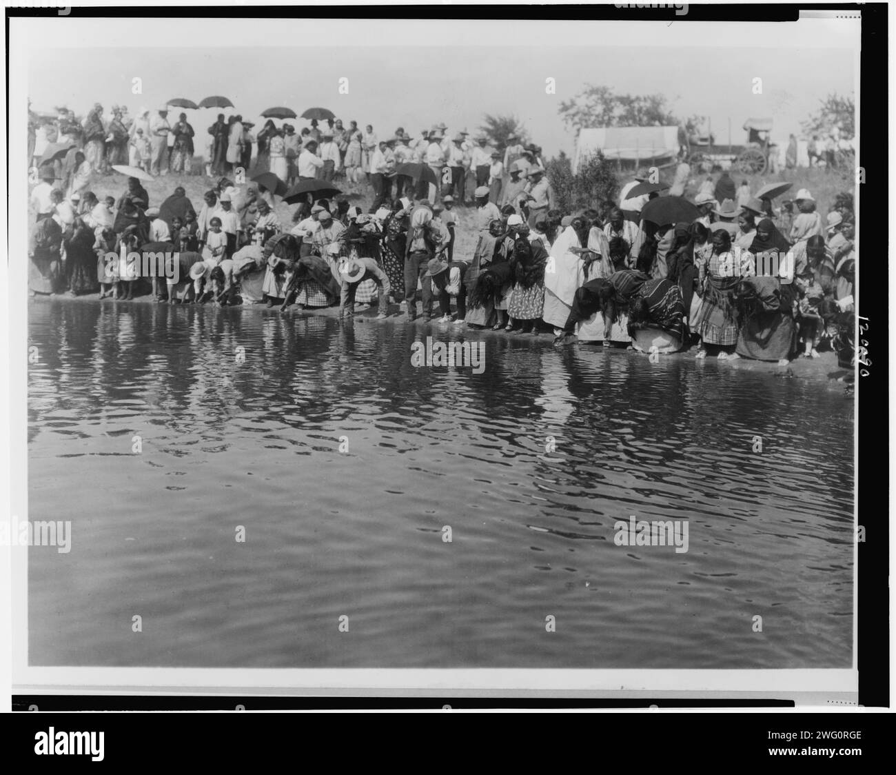 At the pool, animal dance-Cheyenne, c1927. Cheyenne people gathered along waterfront, some dipping hands in water, some carrying umbrellas. Stock Photo