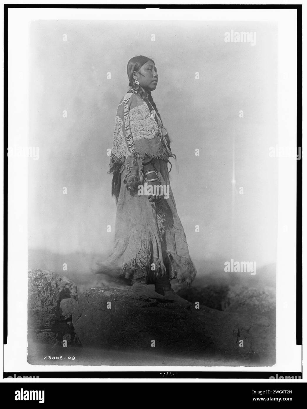 Wishham woman, c1910. Chinookan Indians: Tlakluit; Washington. Landscape, portrait, woman, full length, facing right, standing, wearing beaded buckskin dress. Stock Photo