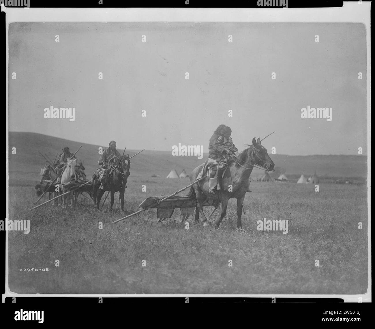 Moving camp-Atsina, c1908. Several Atsina on horses with travois behind them, tipis in background. Stock Photo