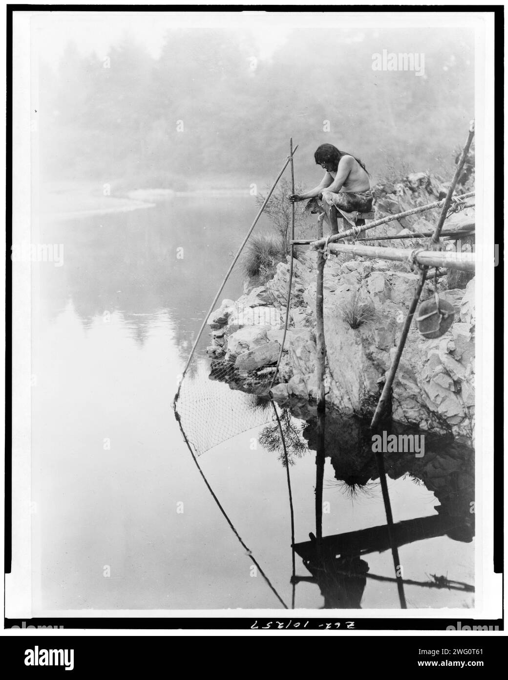 Fishing from a platform, c1923. Hupa Indian on platform over water using fishing net. Stock Photo