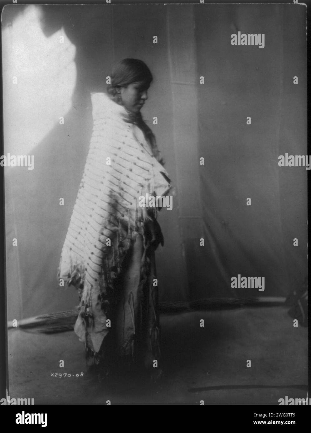 Atsina maiden, c1908. Atsina woman, full-length portrait, standing, facing right. Stock Photo