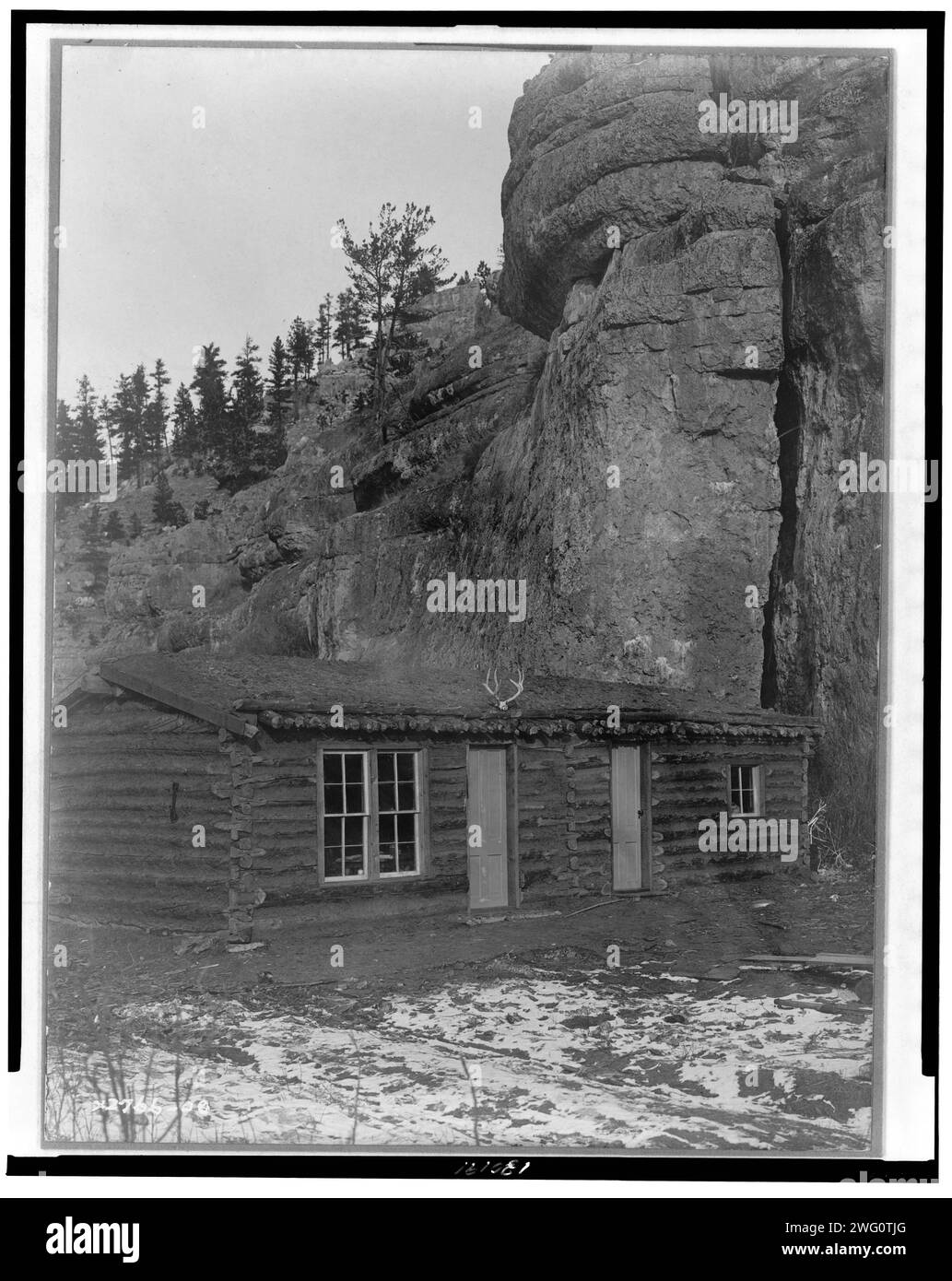 Camp Curtis, c1908. Log cabin in clearing in front of a large rock formation. Stock Photo