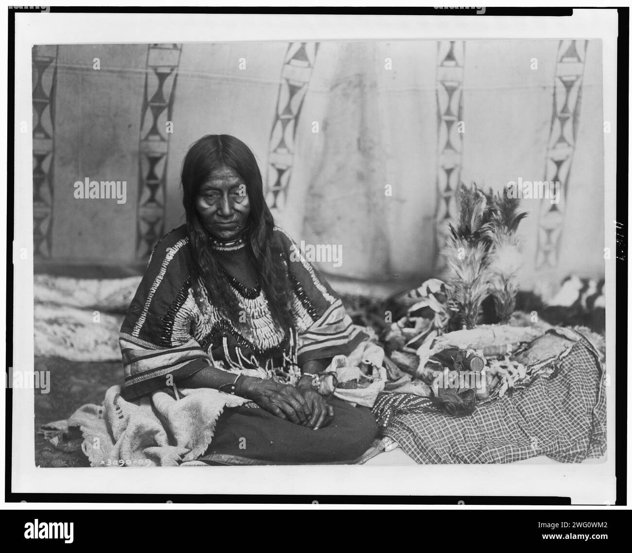 Two Kill, c1910. Piegan woman, full-length portrait, seated on blankets inside tipi(?), facing front. Stock Photo