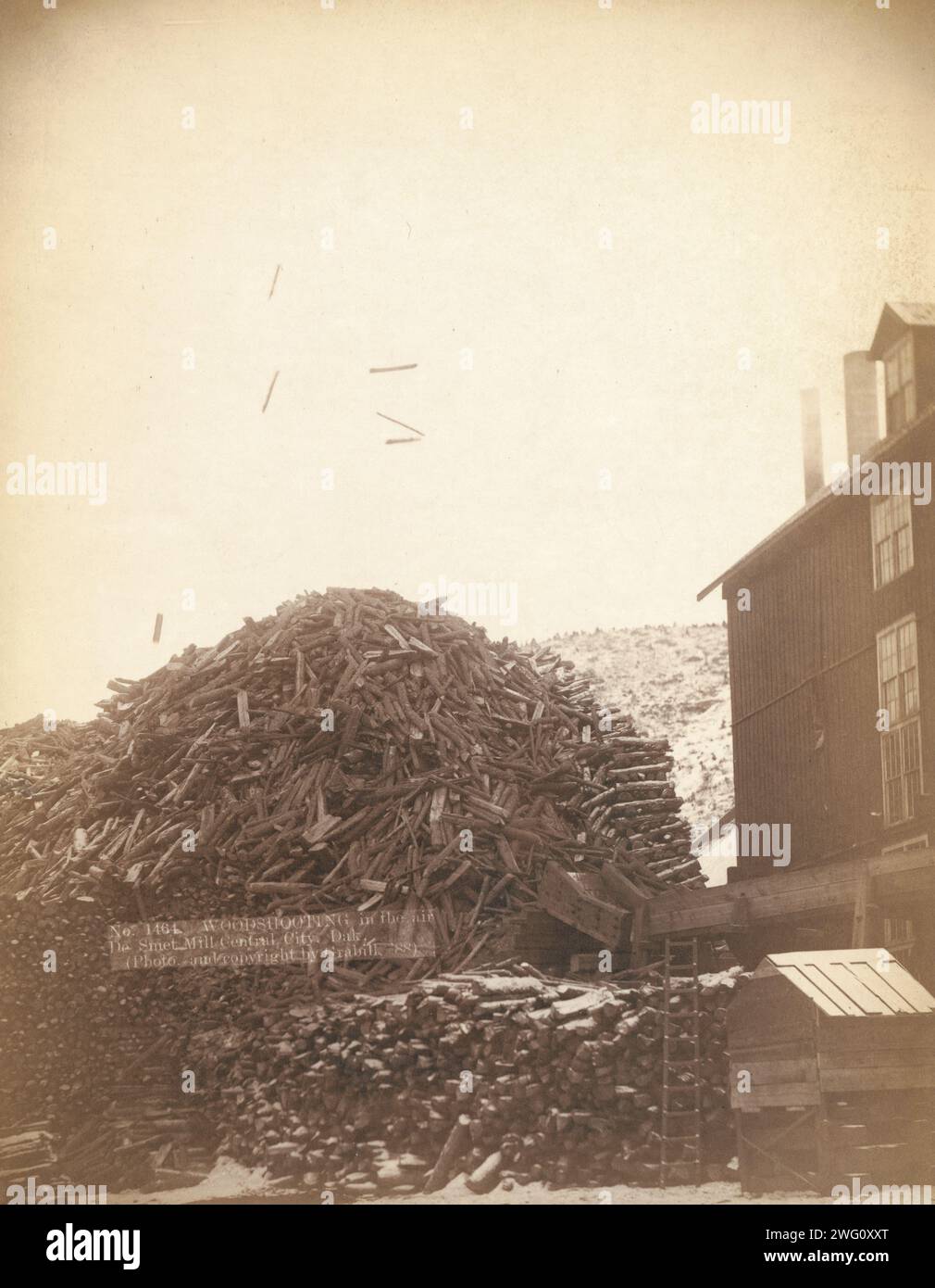 Wood shooting in the air, De Smet Mill, Center City, Dak, 1888. Large pile of timber next to a building. Stock Photo
