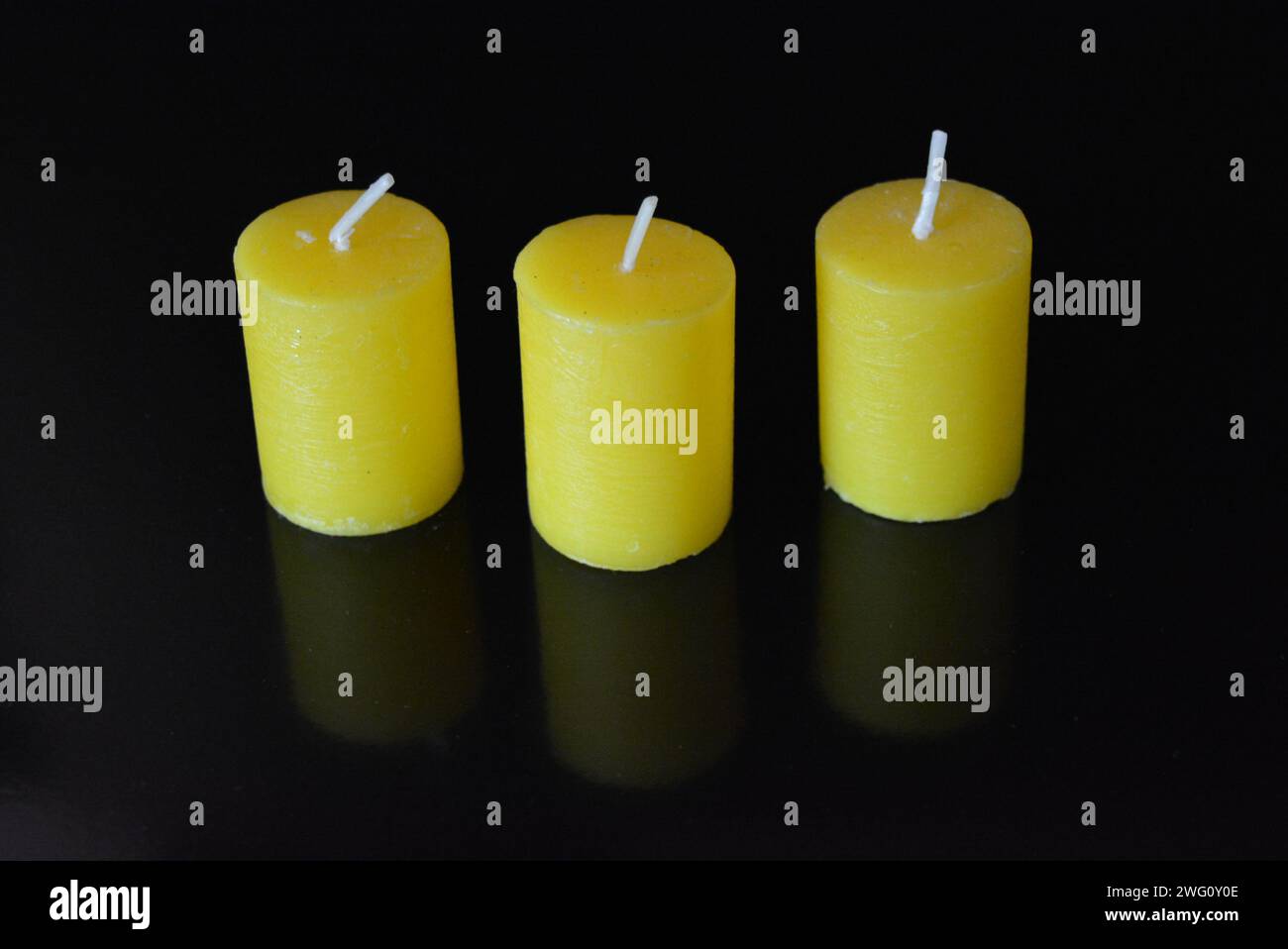 Home furnishings, yellow bright candles placed on black glossy background. Stock Photo