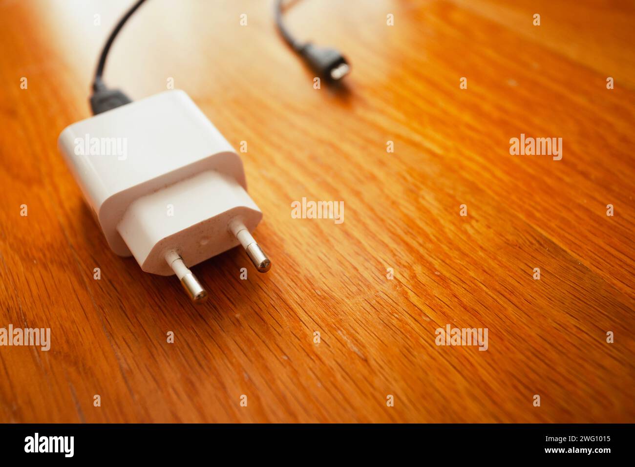 A white smartphone charger lies on the wooden brown floor Stock Photo