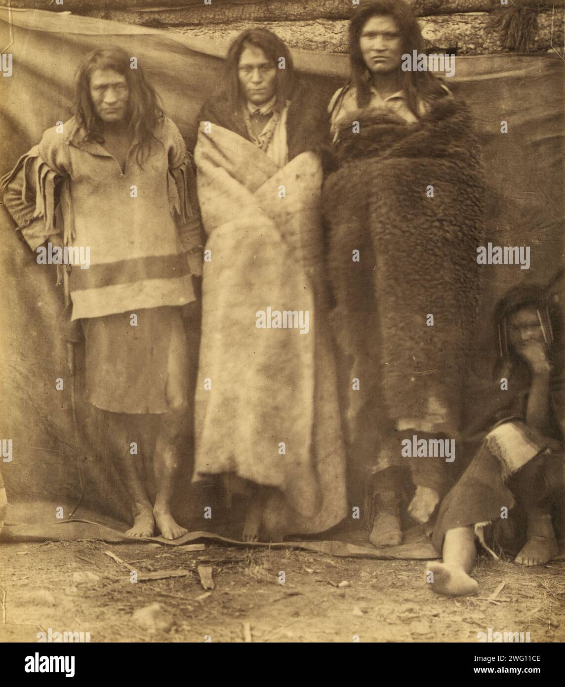 Group of Native Americans, three standing, one seated on the ground, possibly Colville or Kutenai, at the winter quarters of the British Northwest Boundary Commission Survey in Colville, Washington, 1860 or 1861. In: Photographs of British Northwest Boundary Survey, 1858-1861. Stock Photo