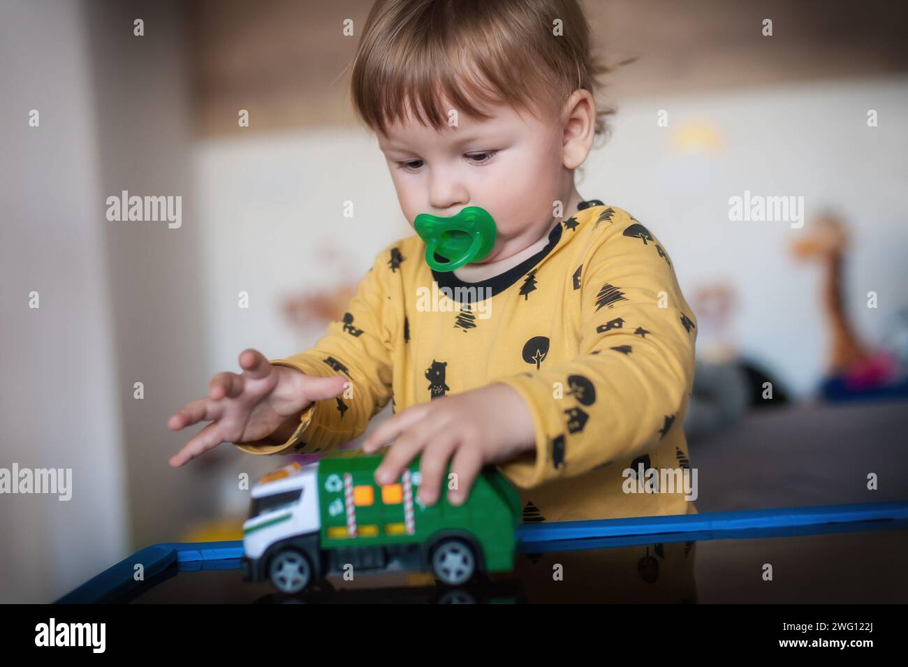 Cute baby boy with pacifier in mouth plays with a small toy truck, driving it around a make-believe world filled with excitement and wonder Stock Photo