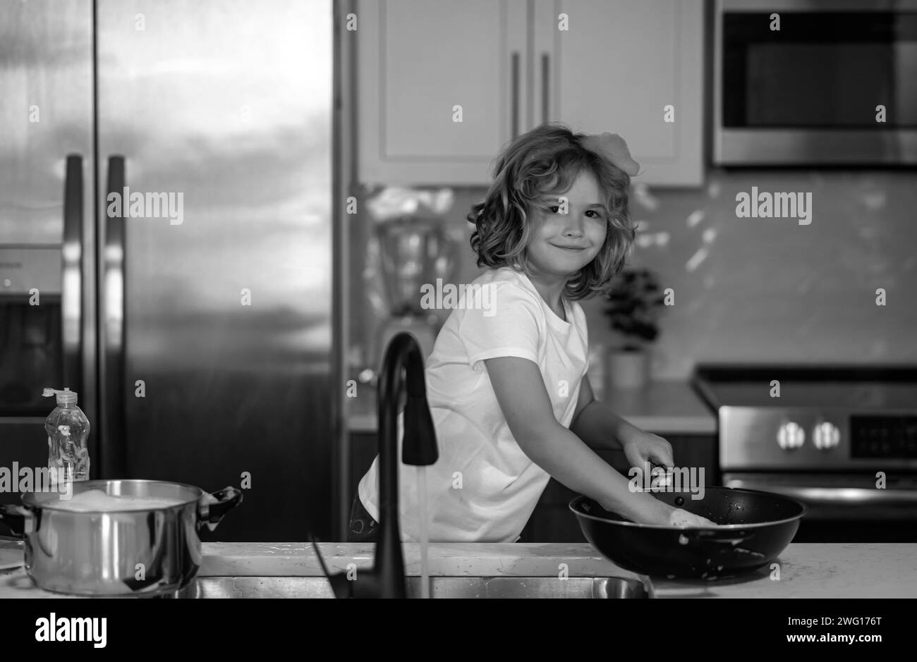 Portrait of a 7-8 years old boy washing the dishes at home. Child boy washing dishes in the kitchen interior. Child helping his parents with housework Stock Photo