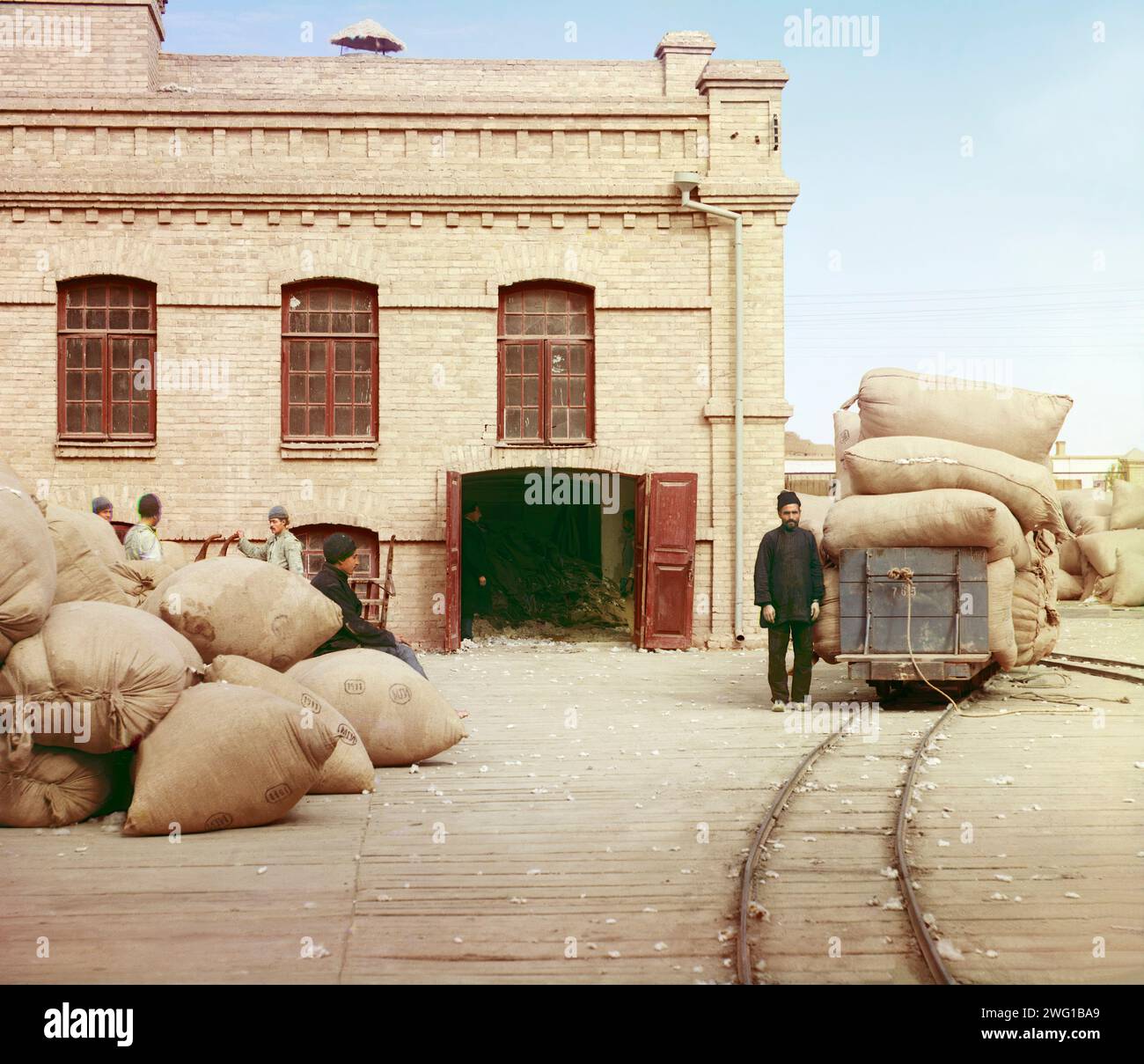 Labourers loading sacks onto railway at factory warehouse, [Russia/Central Asia?], between 1905 and 1915. The sacks are probably filled with raw cotton. Stock Photo