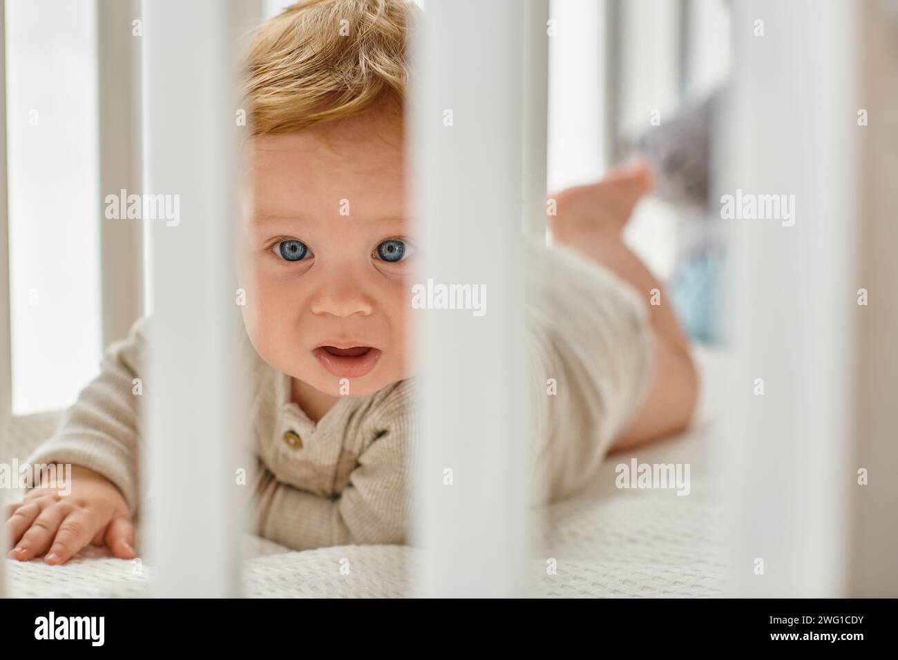 Blueeyed infant baby boy peeking through crib slats in his nursery