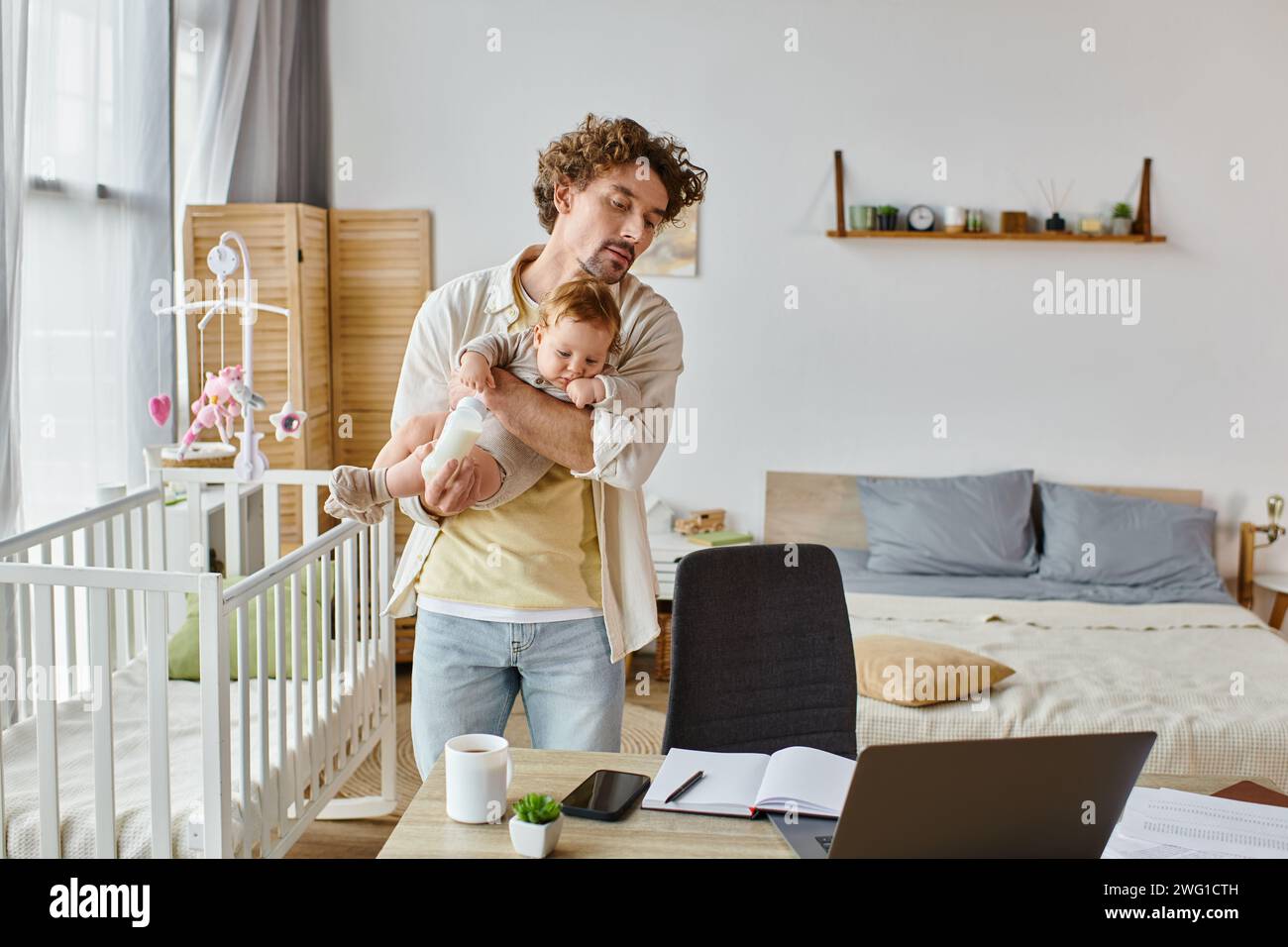 caring single father holding son with baby bottle and looking at laptop ...