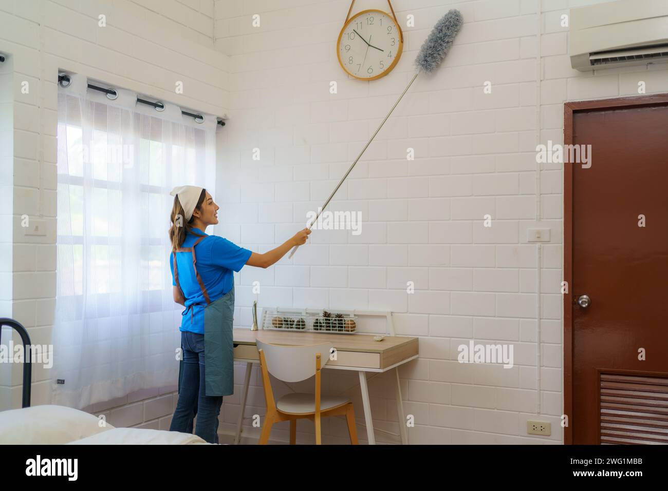 Company housekeepers as they meticulously use dust brushes to clean and refresh the walls in a bedroom thoroughness and commitment of the cleaning tea Stock Photo