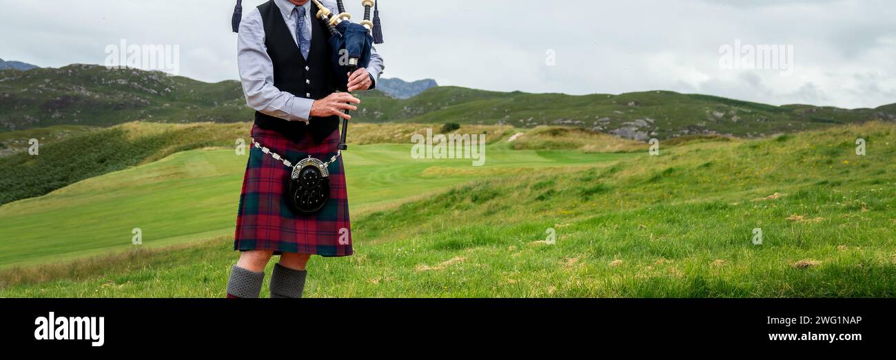 Scottish bagpiper in the Highlands of Scotland, panoramic mountains landscape background, UK Stock Photo