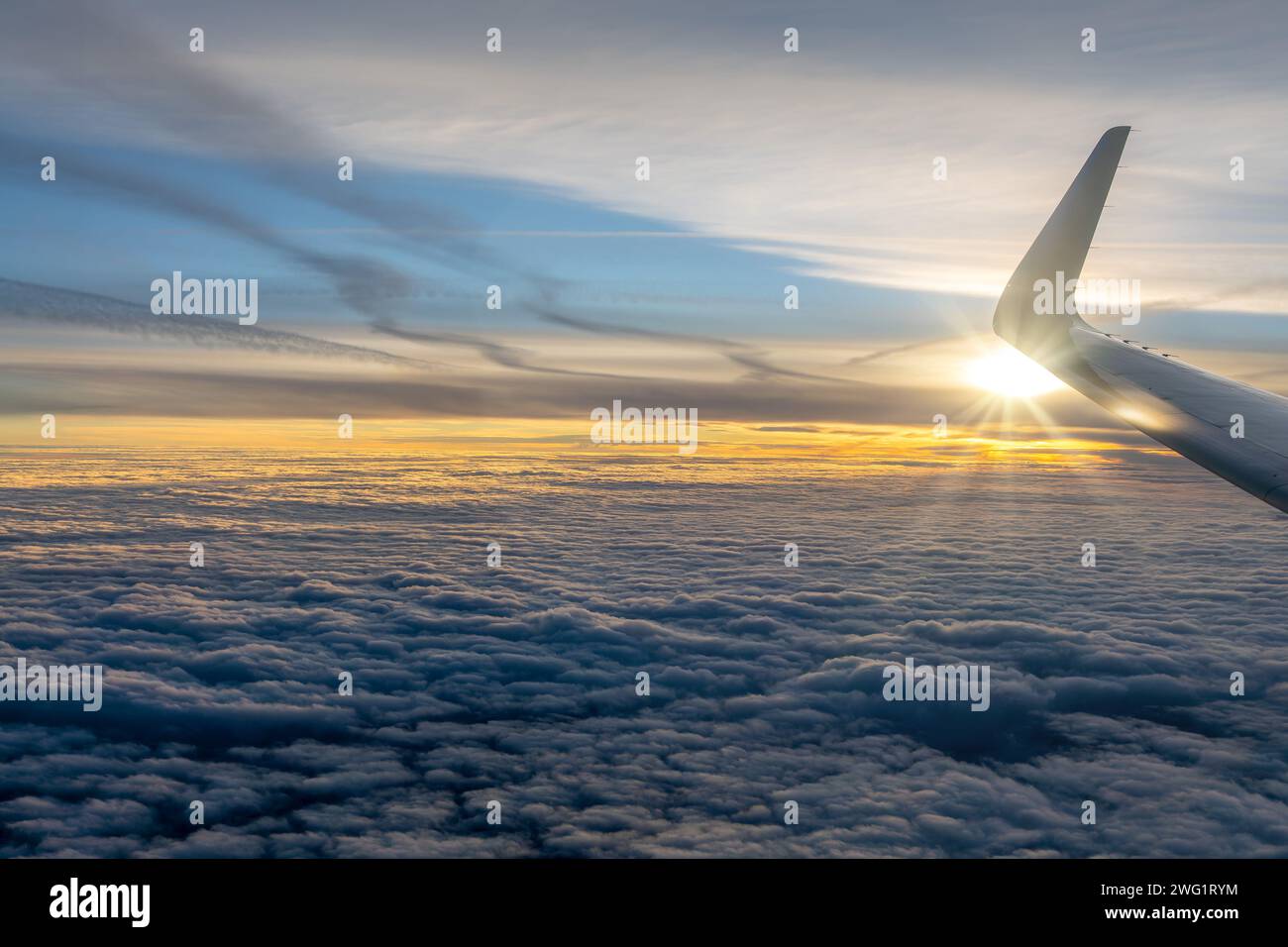 View from an airplane window over a sea of clouds at sunset with the plane wing Stock Photo