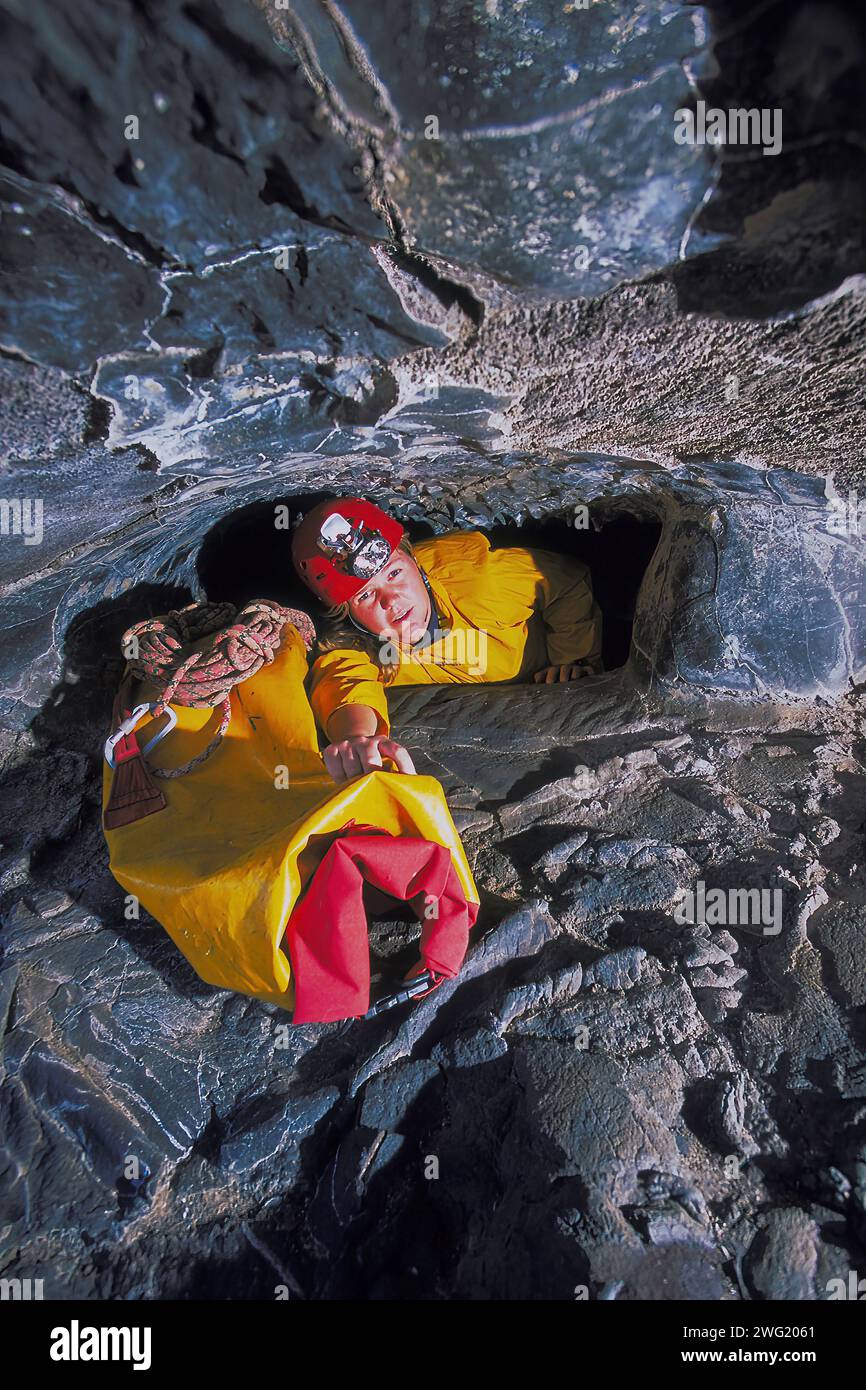 Female caver negotiating a tight, narrow crawl in a volcanic lava tube cave. Big Island, Hawaii. Stock Photo